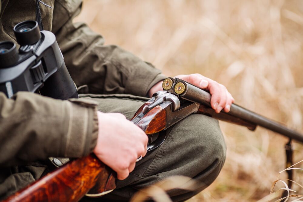 Person in field clothing holding an open side-by-side shotgun
