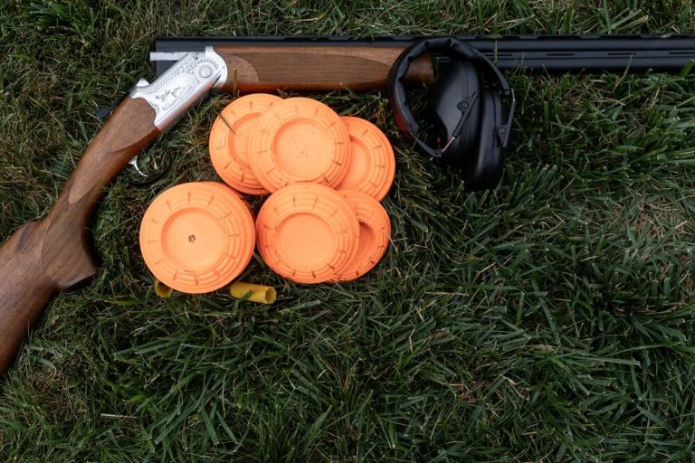 Over-and-under shotgun, orange clay pigeons and ear defenders on grass