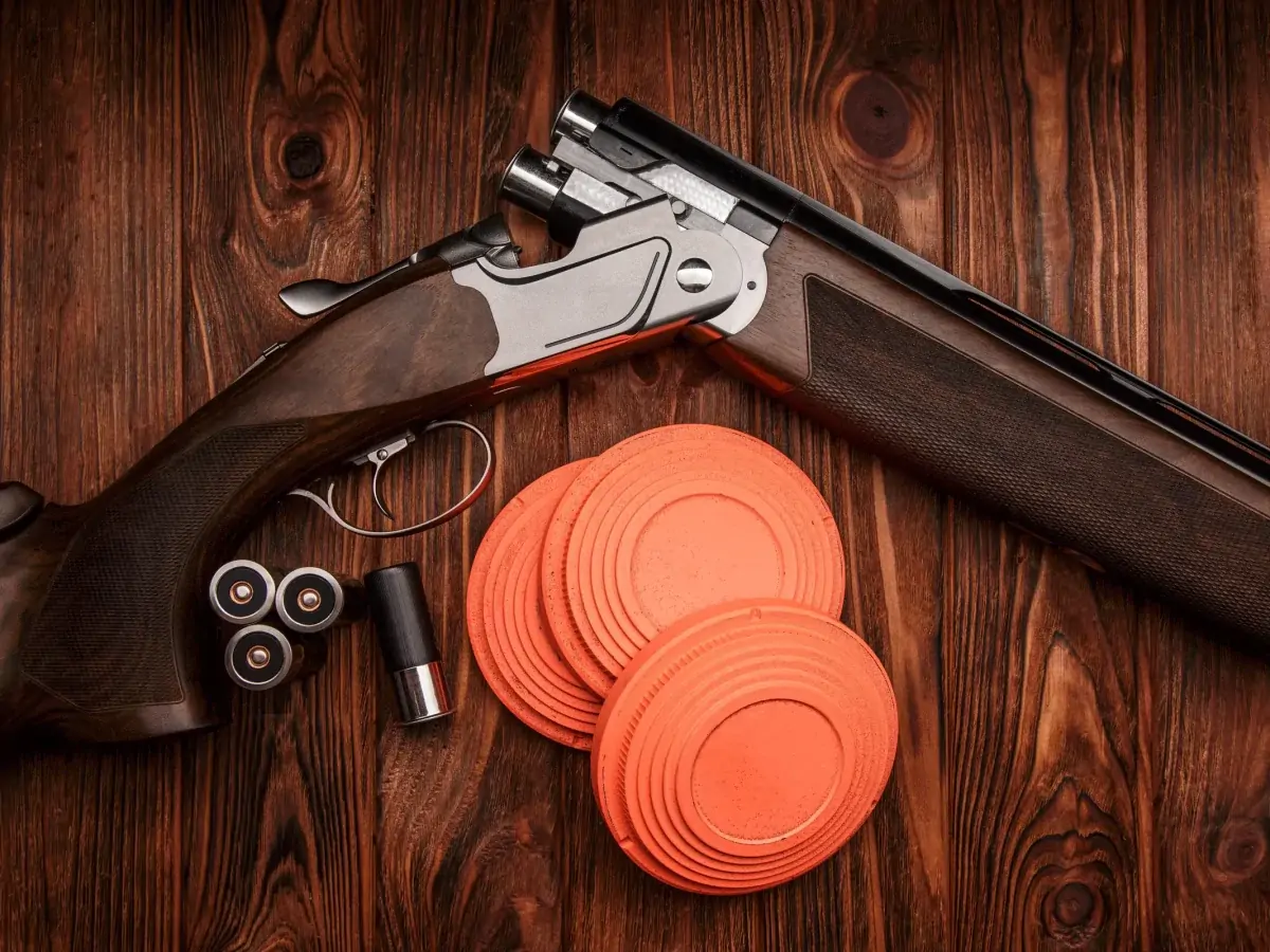 Shotgun, cartridges and orange clay pigeons on wood