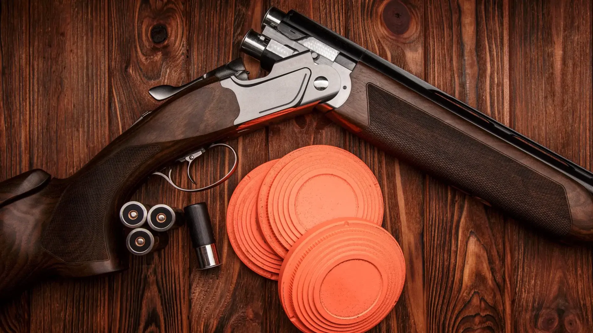 Shotgun, cartridges and orange clay pigeons on wood