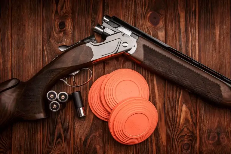 Shotgun, cartridges and orange clay pigeons on wood